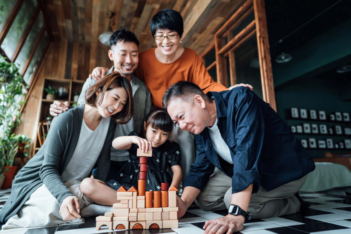 joyful multi generation asian family, grandparents, parents and kid sitting on the floor in the living room having fun playing wooden building blocks together at home